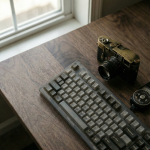 A high-end mechanical keyboard and vintage camera clustered on a walnut desk, illustrating the Gestalt Principle of Proximity in unified brand messaging.